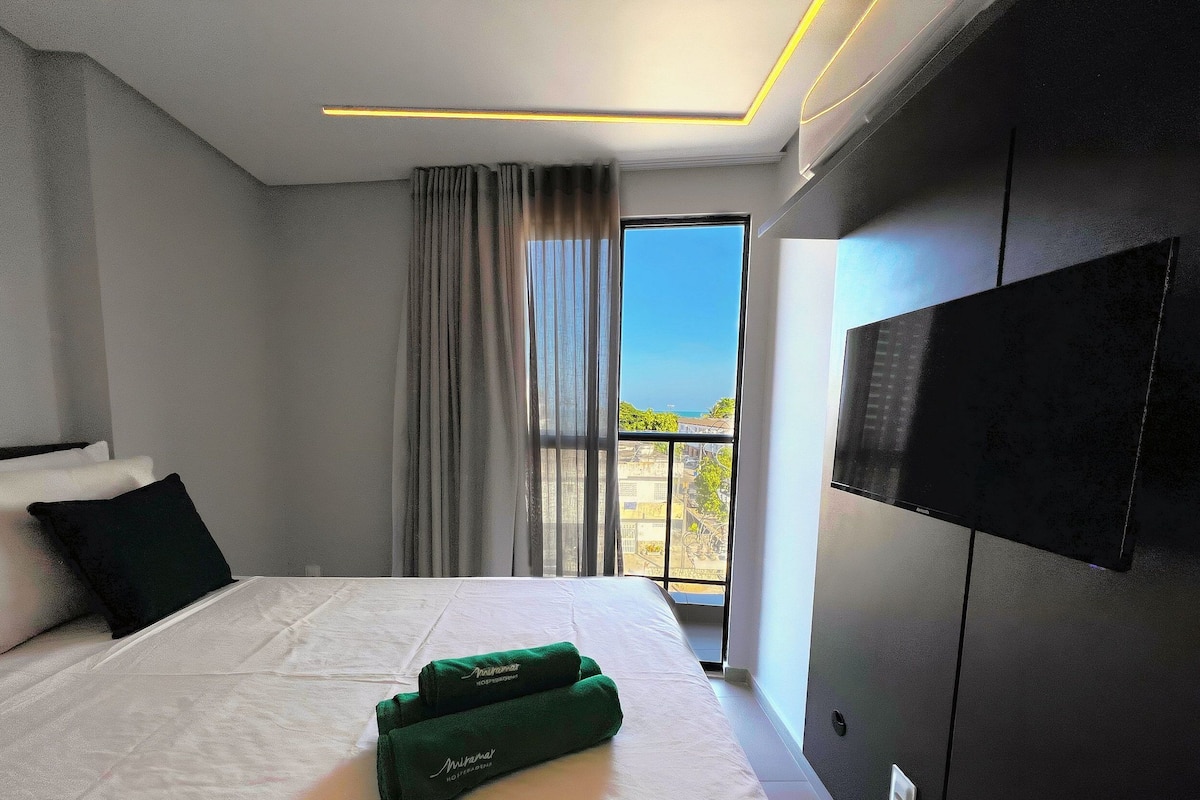 A modern hotel room with a large bed, a flat-screen TV, and a view of the outdoors.