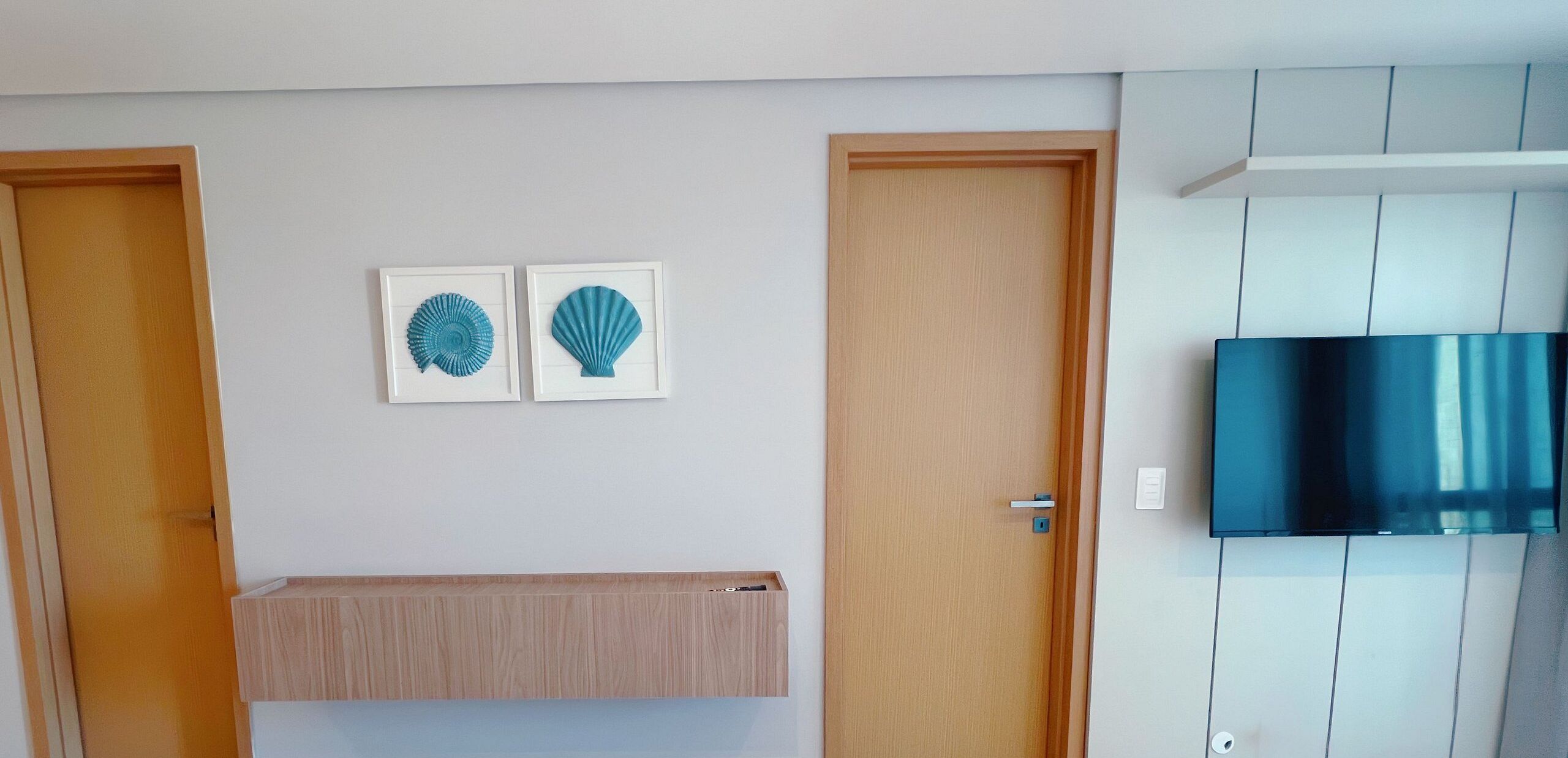 A room with two doors, a mounted TV, and two framed wall decorations.