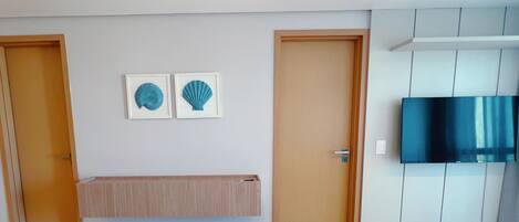 A room with two doors, a mounted TV, and two framed wall decorations.