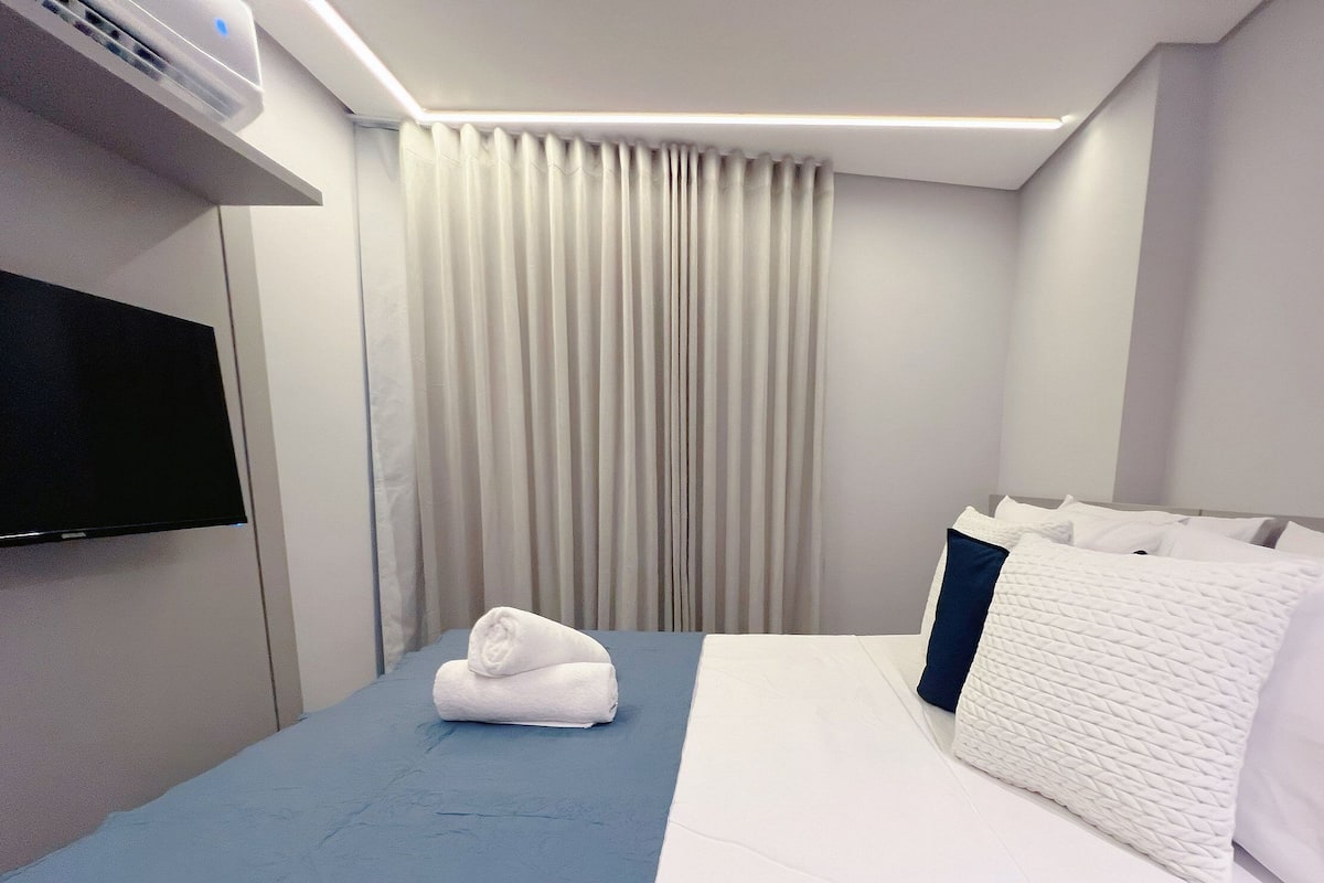A hotel room with a bed, a TV mounted on the wall, and a window with curtains.