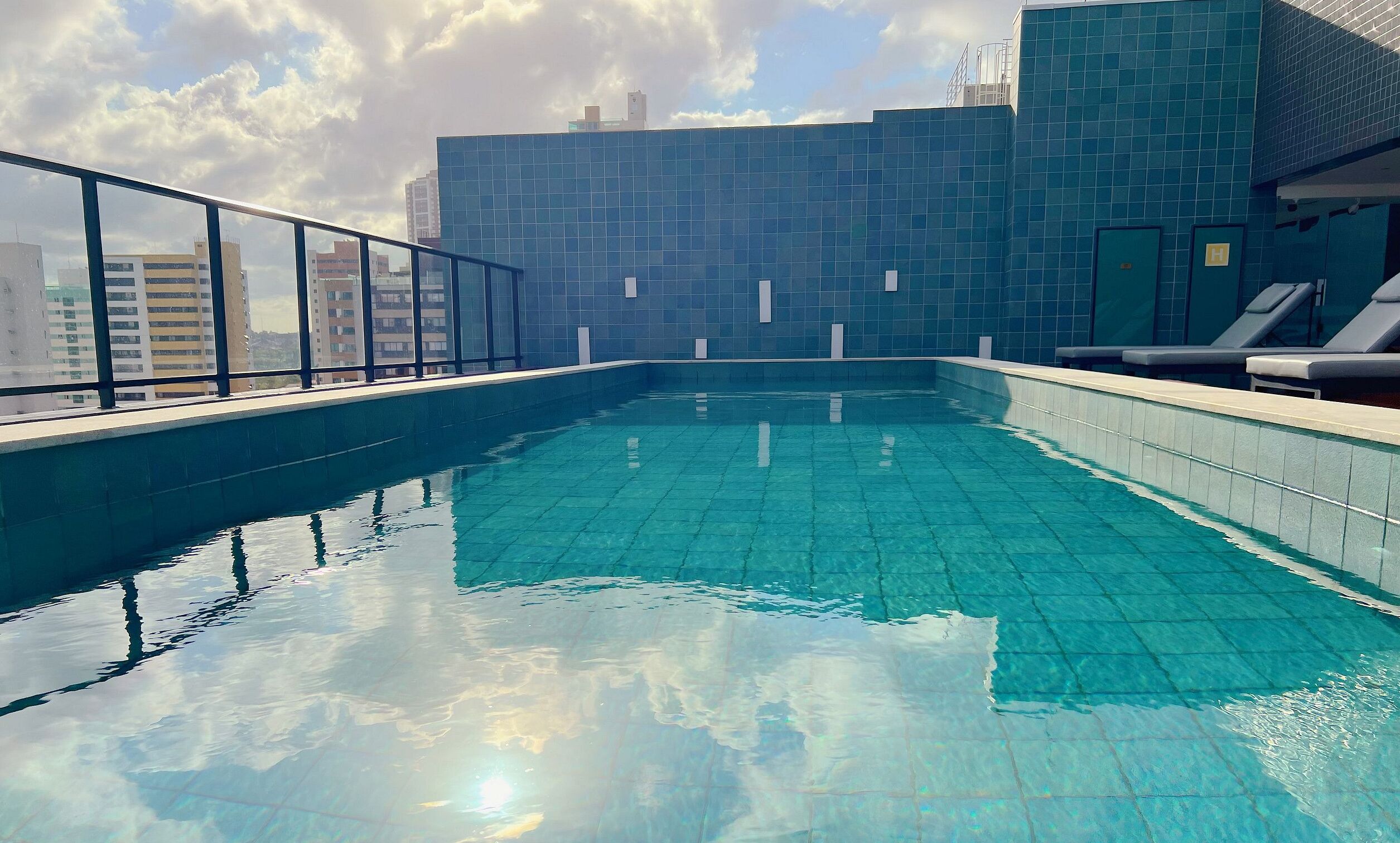 Ein Hallenbad mit klarem, blauem Wasser, umgeben von einer Kachelwand und einem Glasgeländer.