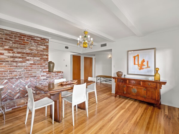 A dining area with a brick wall, wooden dining table, white chairs, and a wooden cabinet with a framed artwork. - Mid-Mod Storybook Ranch Near Fig Garden Village (Fresno)