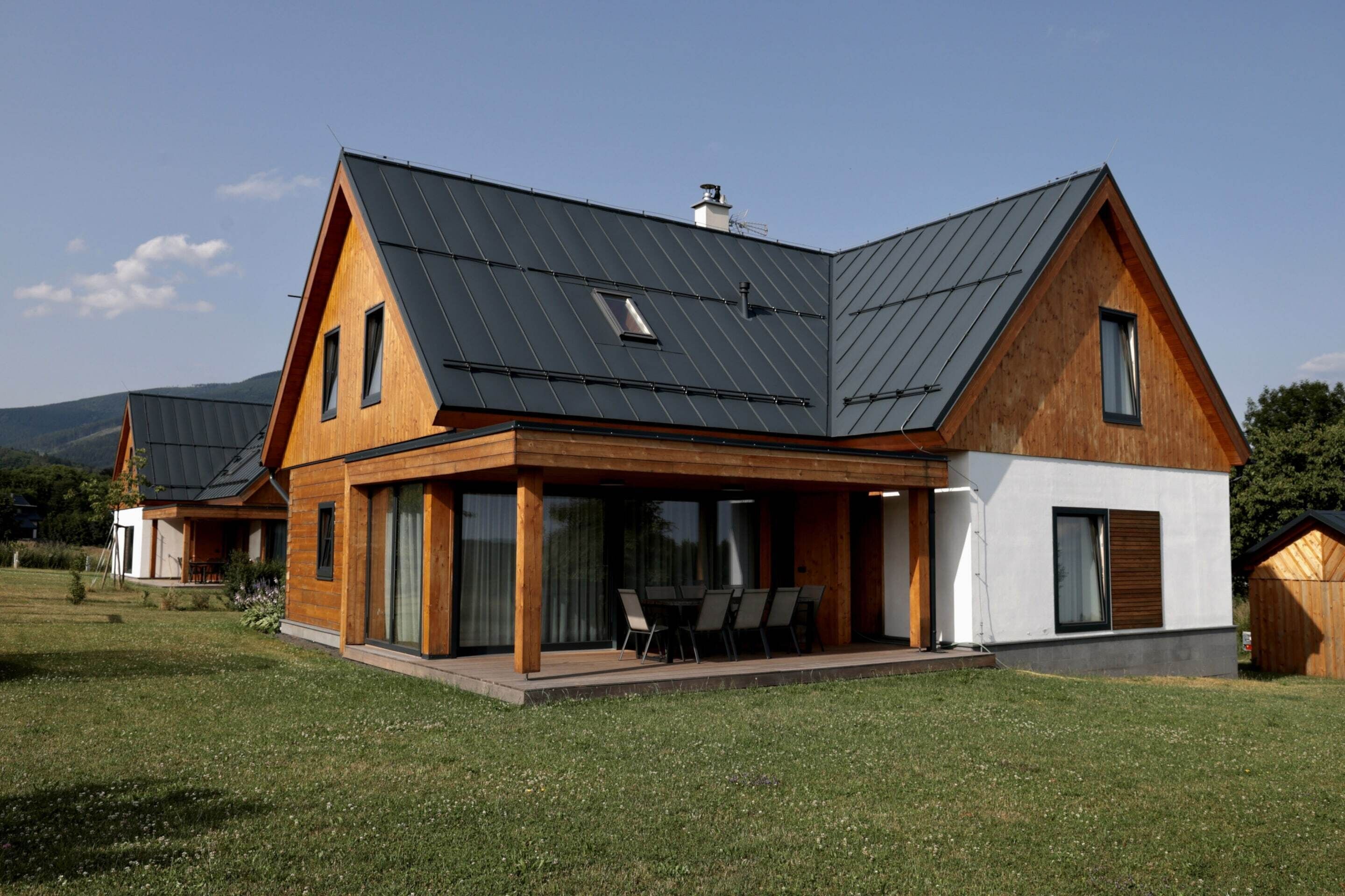 Ein modernes Haus mit geneigtem Dach, großen Fenstern und einer überdachten Terrasse.