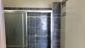 Een badkamer met een douchecabine van glas, betegelde wanden en een deur.