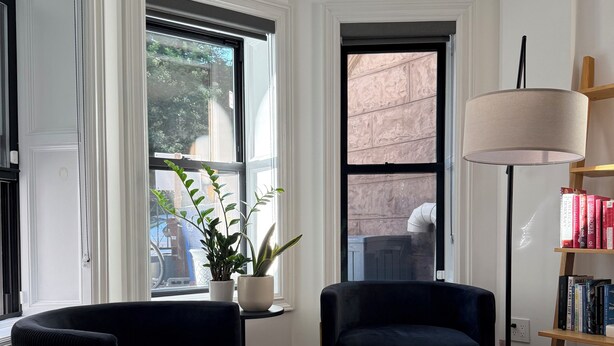 Un salon moderne avec deux canapés sombres, une petite table ronde, un tapis blanc et un lampadaire.