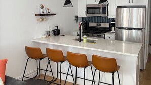 Une cuisine moderne avec des meubles blancs, des appareils en acier inoxydable et un îlot central doté de tabourets de bar.
