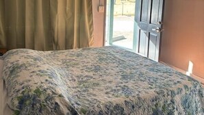 A bedroom with a bed, a ceiling fan, a door, and curtains. - Black Hawk Lodge (Coarsegold)