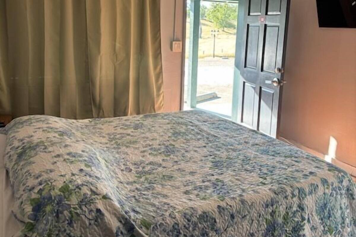 A bedroom with a bed, a ceiling fan, a door, and curtains.
