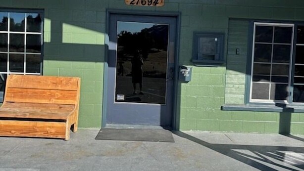 A building with a green exterior, a wooden bench outside, and a door with the number 27694. - Black Hawk Lodge (Coarsegold)