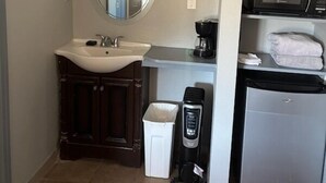 A compact bathroom with a sink, mirror, and a small coffee maker. - Black Hawk Lodge (Coarsegold)