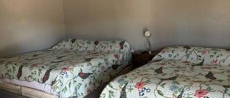 Quarto com duas camas, cada uma com roupa de cama floral e um ventilador de teto.