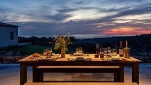 Mesa de comedor lista para una comida con vistas a la puesta de sol sobre un paisaje montañoso.