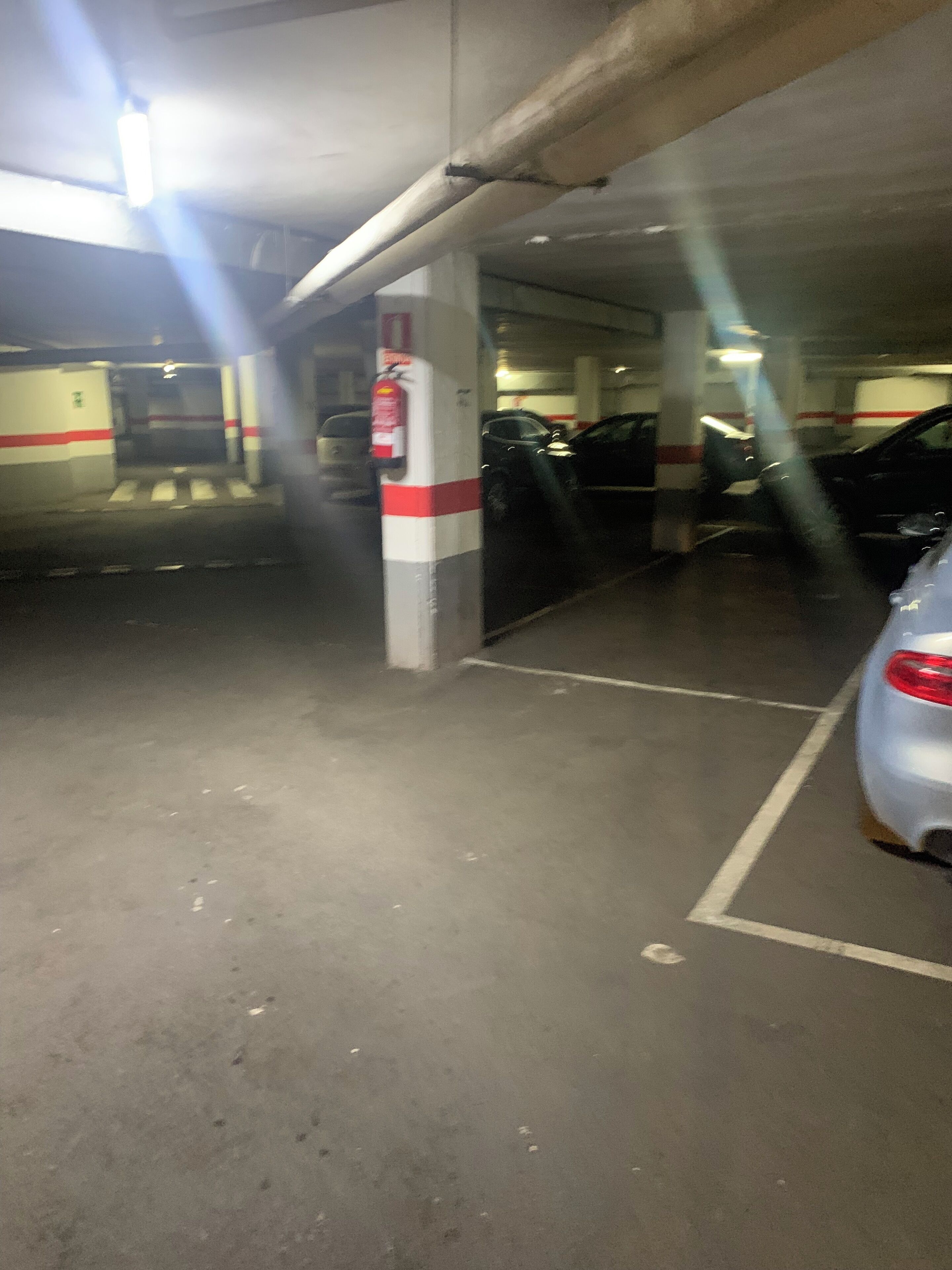 Een ondergrondse parkeergarage met betonnen pilaren, aangegeven parkeerplaatsen en een brandblusser bevestigd aan een pilaar.