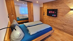 A modern bedroom with a wooden wardrobe, a bed with blue bedding, and a wall-mounted TV displaying the Netflix logo. - Apartment Hipp No. 8 - 74m² new building on the 1st floor with balcony and mountain view in a top location (Halblech)
