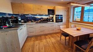 A modern kitchen with wooden cabinets, a built-in oven, and a dining area with a wooden table and chairs. - Apartment Hipp No. 8 - 74m² new building on the 1st floor with balcony and mountain view in a top location (Halblech)