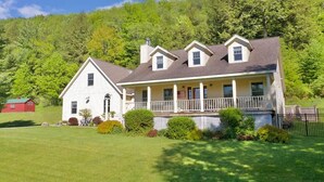 A two-story house with a porch, surrounded by a well-maintained lawn and a forested hillside.