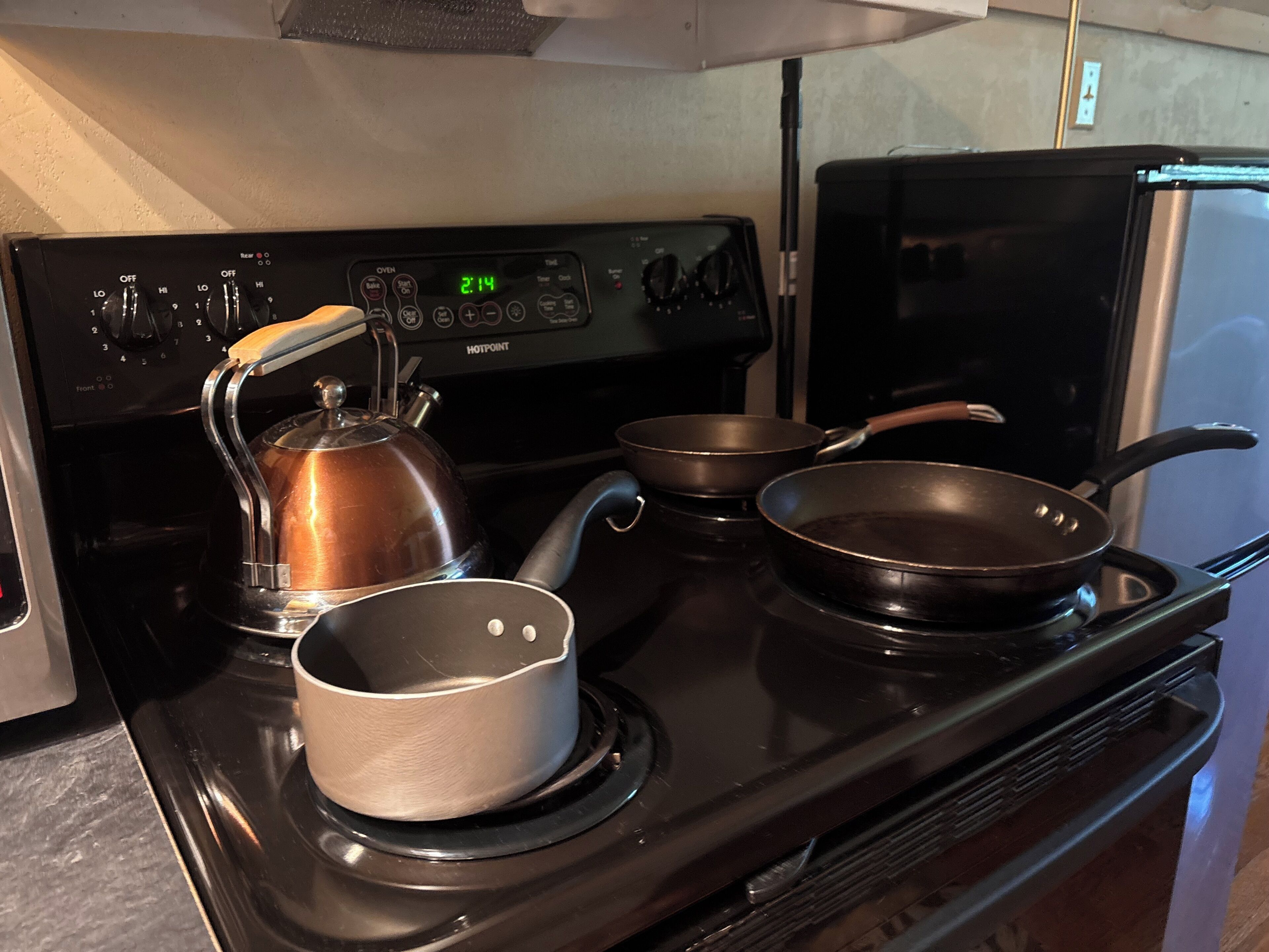 A kitchen with a stove, kettle, and two frying pans.