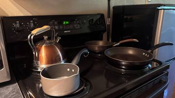 A kitchen with a stove, kettle, and two frying pans.