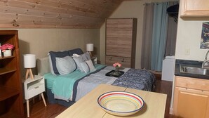 A cozy room with a bed, bedside table, and a small kitchen area.
