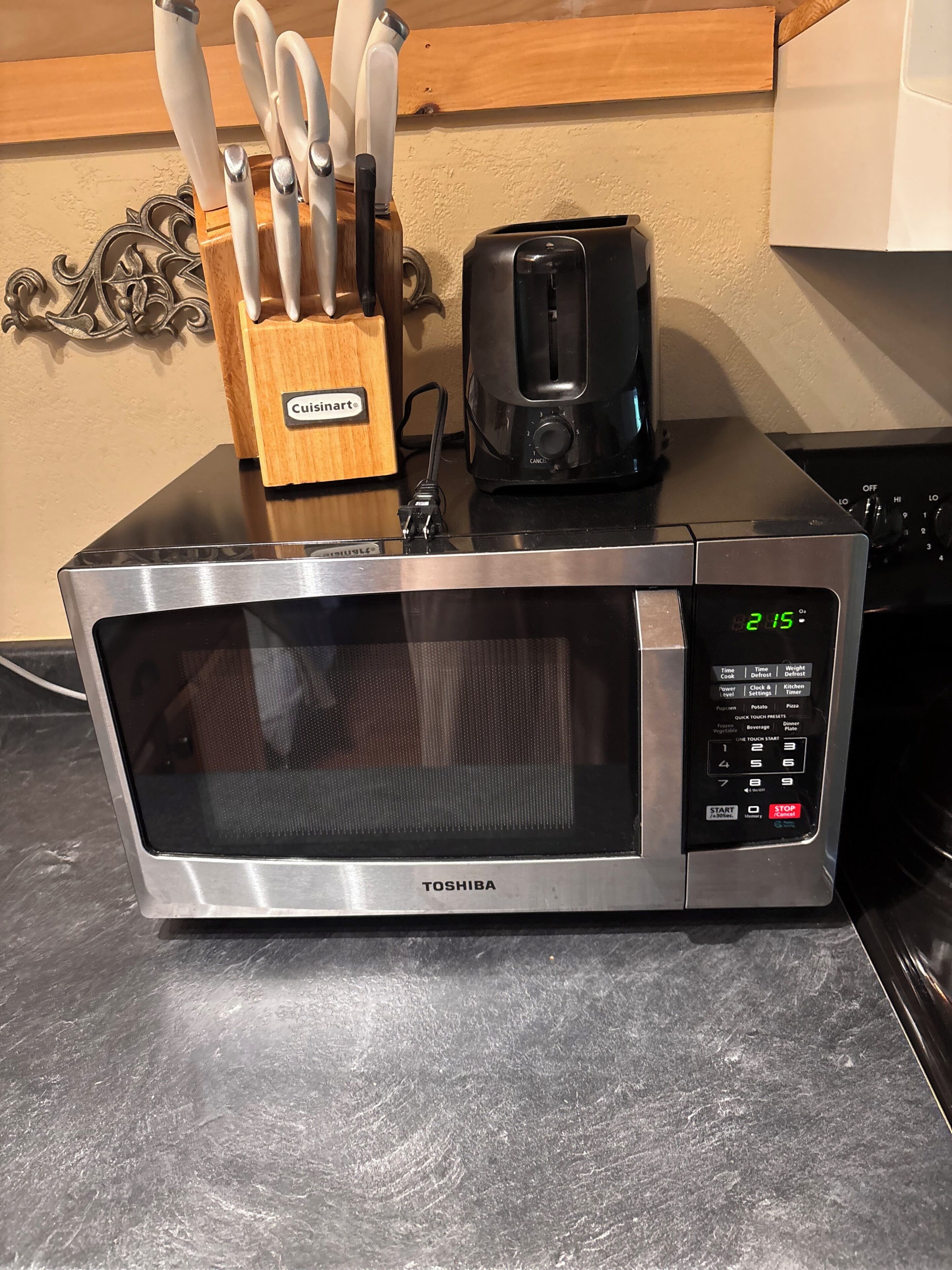 Eine Toshiba-Mikrowelle mit digitaler Anzeige, ein Toaster und ein Messerblock auf einer Küchenarbeitsplatte.