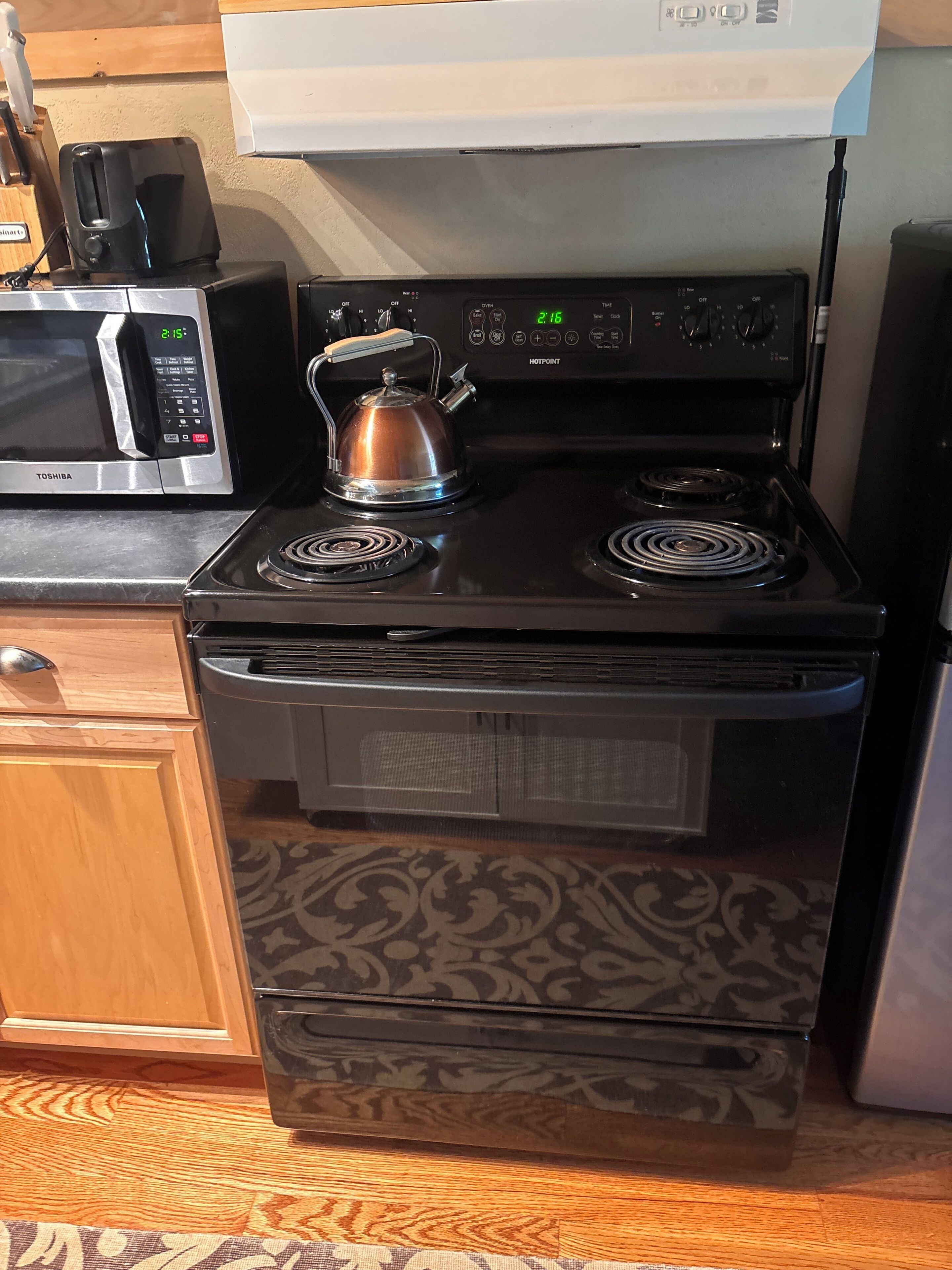 Une cuisine équipée d’une cuisinière noire, d’un four à micro-ondes et d’une bouilloire.