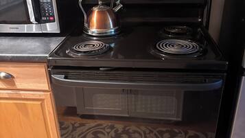Une cuisine équipée d’une cuisinière noire, d’un four à micro-ondes et d’une bouilloire.