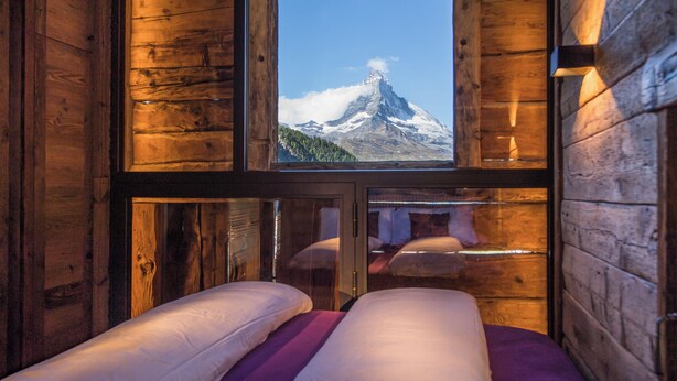 A wooden cabin room with a bed and a window offering a mountain view.
