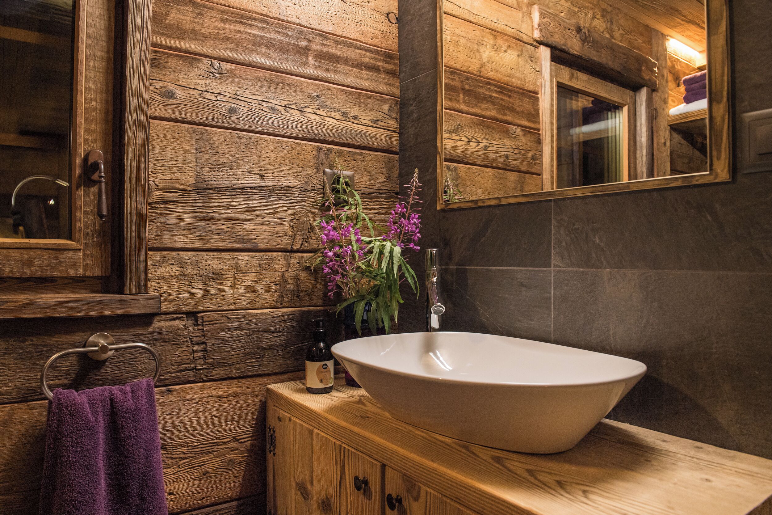 A wooden cabin-style bathroom with a large oval sink, a wooden cabinet, a towel rack, and a mirror.