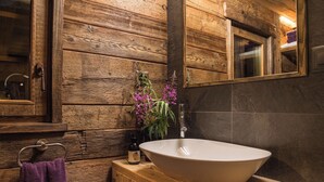 A wooden cabin-style bathroom with a large oval sink, a wooden cabinet, a towel rack, and a mirror.