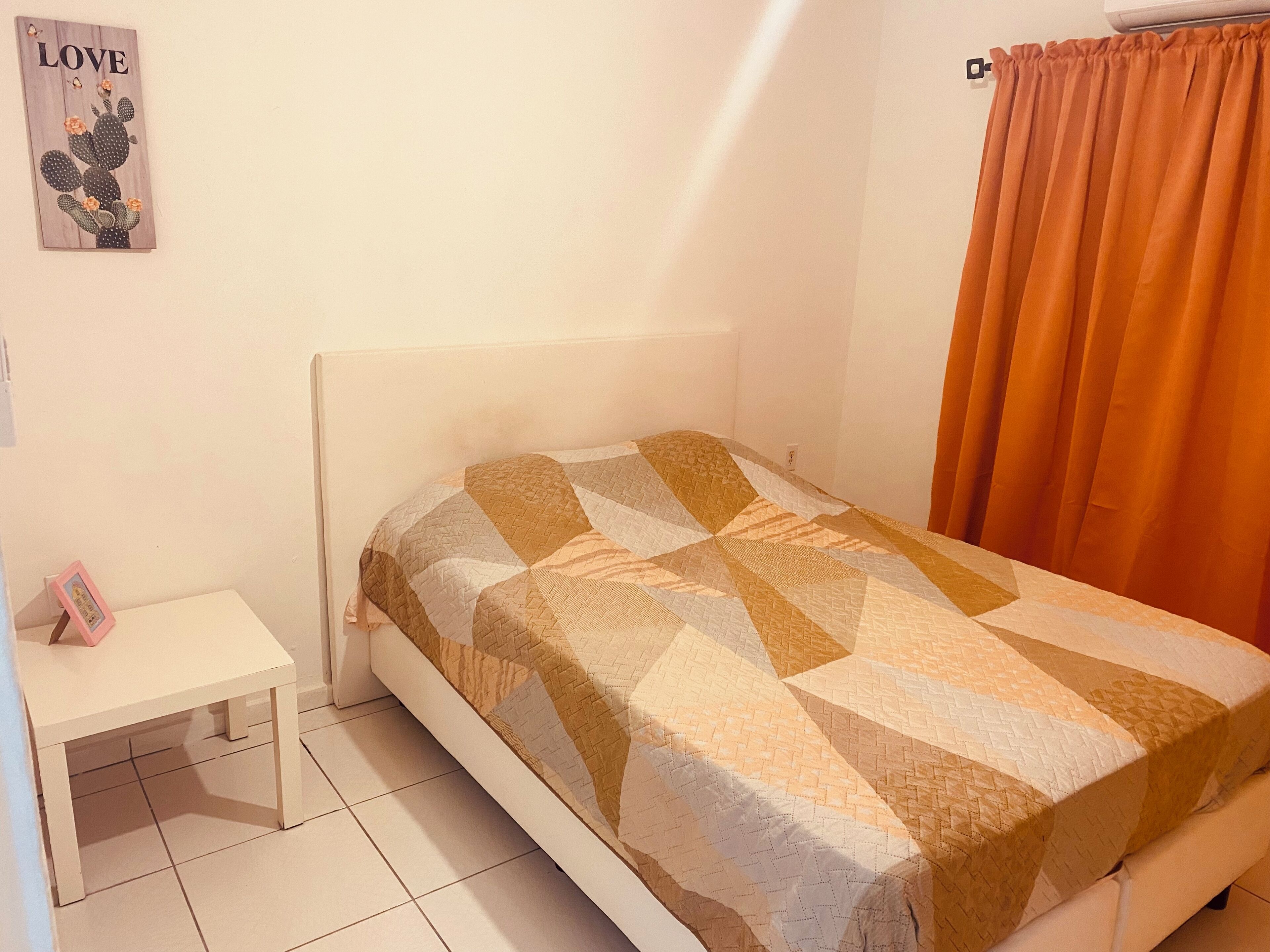 A bedroom with a bed, a nightstand, a wall decoration, and a window with curtains.