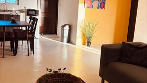 A modern living room with a sofa, a dining area with a table and chairs, a kitchen with a microwave, and a wall with colorful artwork. - Sol appartments with pool (Willemstad)