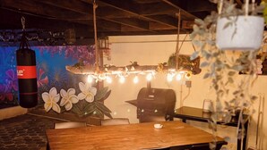 An outdoor dining area with a wooden table and chairs, a hanging light fixture, and a punching bag in the background. - Sol appartments with pool (Willemstad)