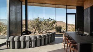 A modern kitchen with a large island, stone seating, and a view of the desert landscape. - Obsidian - Industrial-Modern Villa (Yucca Valley)