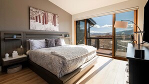 Une chambre avec un grand lit, une table de chevet, une lampe, un tableau au mur et une vue à travers une porte coulissante.