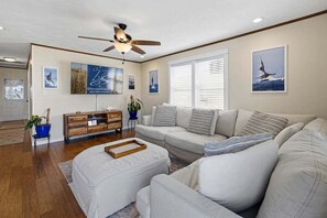 A living room with a sofa, ottoman, wooden sideboard, ceiling fan, and wall art.