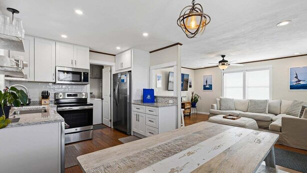 A modern kitchen with white cabinetry, a central island, and a dining area with a rustic table.