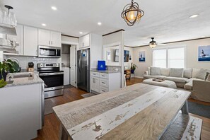 Una cocina moderna con armarios blancos, una isla central y un comedor con una mesa rústica.