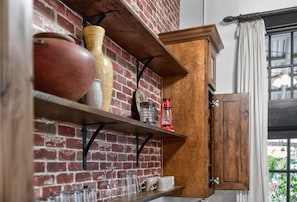 A kitchen with a brick wall, wooden shelves, and a cabinet.