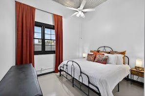 A bedroom with a bed, a desk, a window with curtains, a ceiling fan, and a nightstand with a lamp. - Historic Firehouse within a short stroll to Downtown Chandler, 2 beds, 1 bath,   (Chandler)