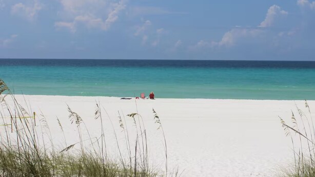 Ein Strand mit weißem Sand und klarem türkisblauem Wasser.