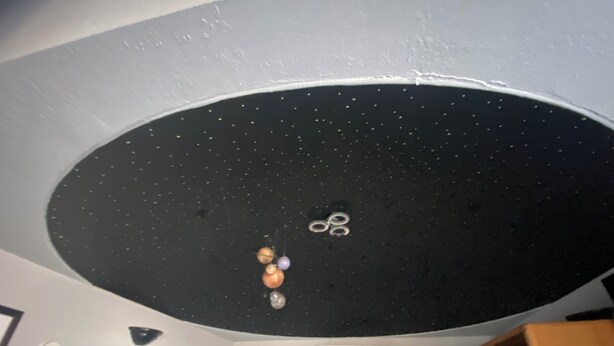 A room with a starry ceiling design, a white air conditioning unit, and a wooden cabinet. - The Galactic Getaway - Lakeside Tiny Home Rental - Queen Bed (Luverne)