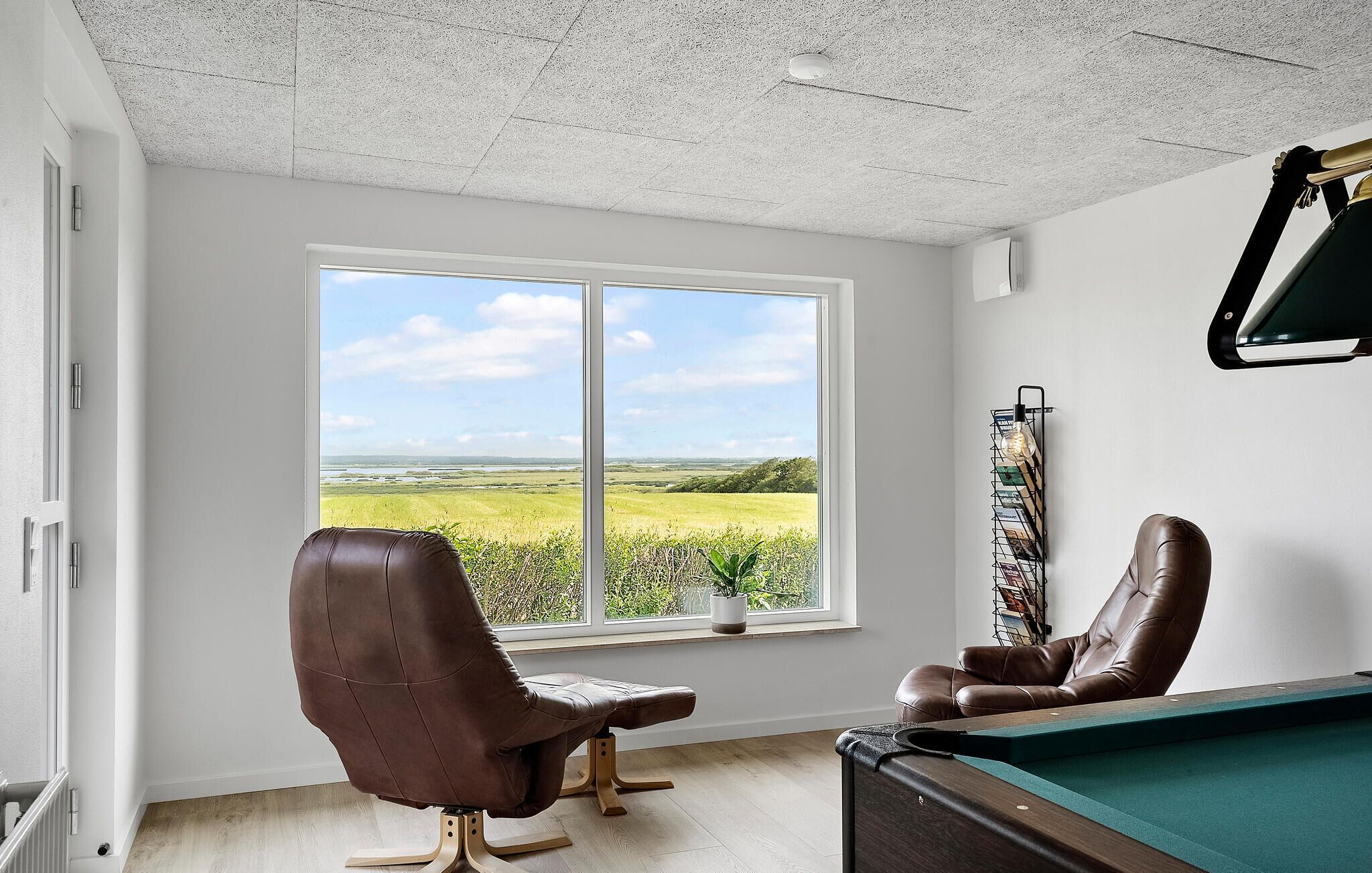 A room with a pool table, a leather chair, and a window with a view of a green field.