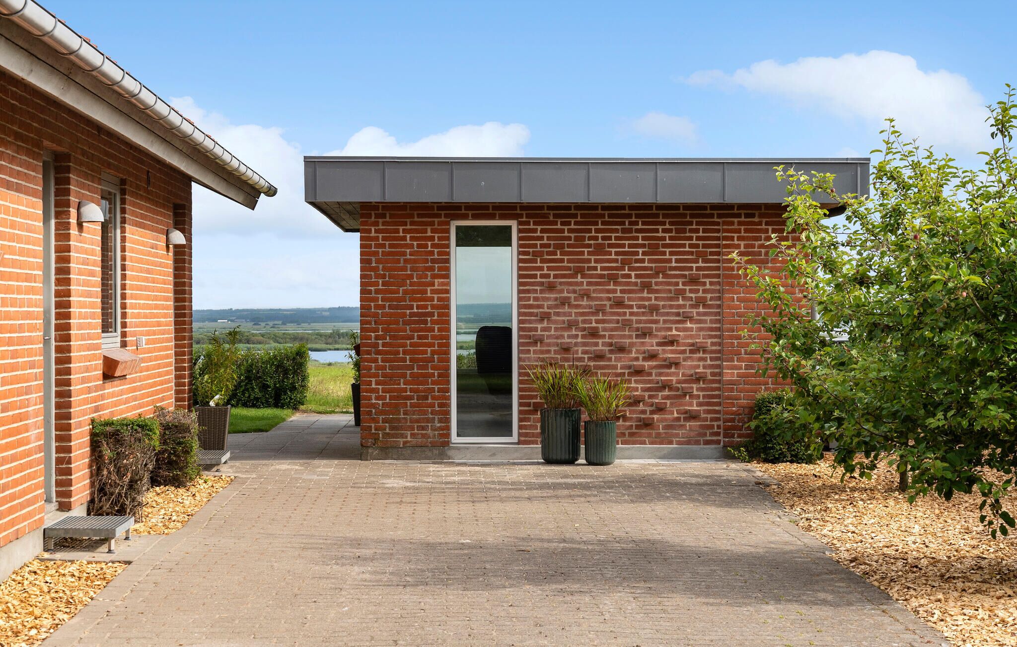 Un bâtiment moderne en briques, doté d’une grande porte vitrée et offrant une vue sur la campagne.