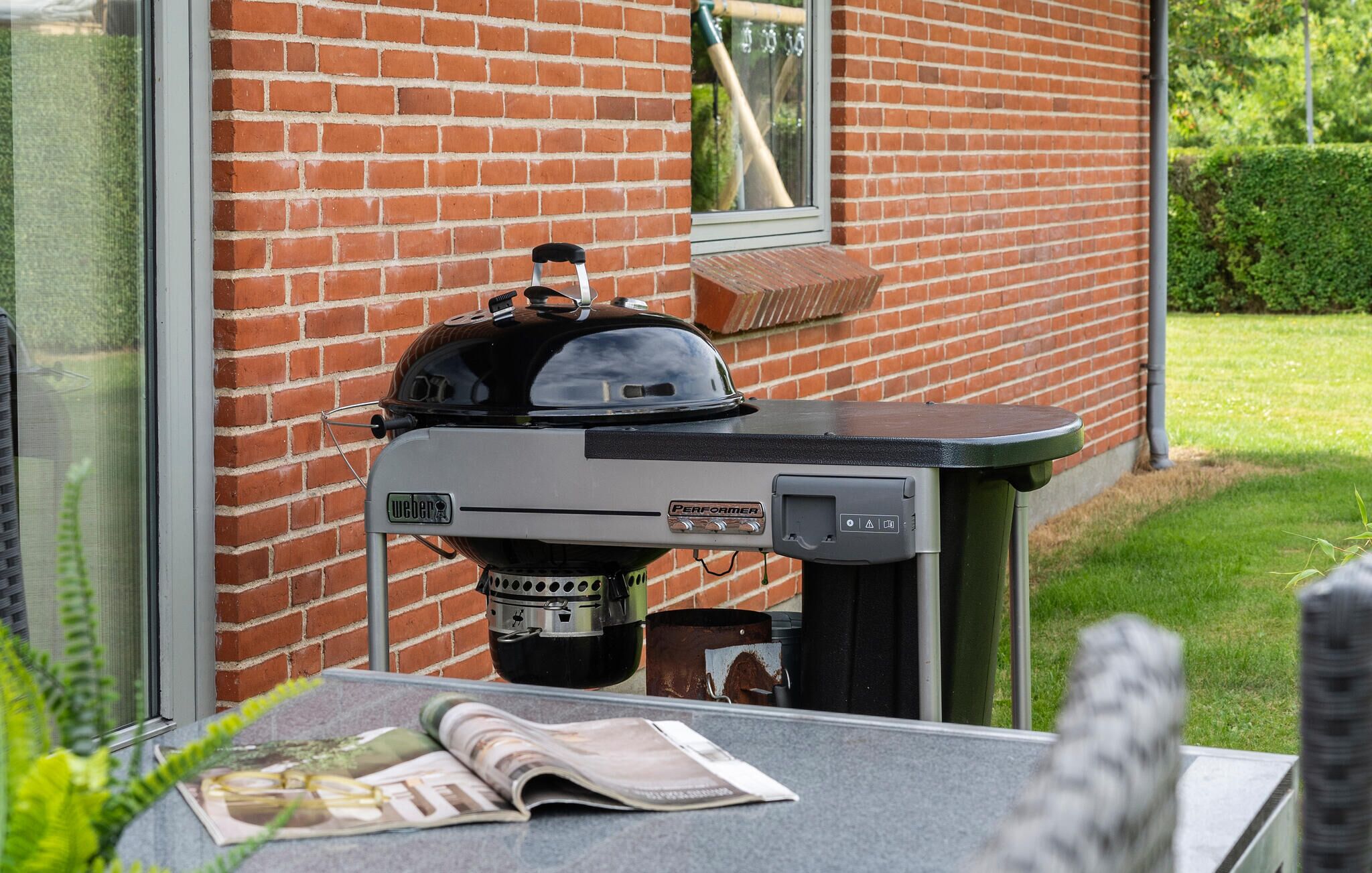 Ein Weber Performer Grill mit schwarzem Deckel und Bedienfeld, auf einem Tisch vor einer Backsteinmauer platziert.