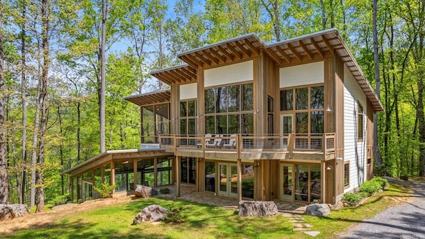 Una moderna casa a due piani in legno, con ampie finestre, un balcone e un vialetto in pietra che conduce all'ingresso.