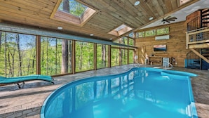 Un interno in legno con una grande piscina, lucernari e vista sulla foresta.