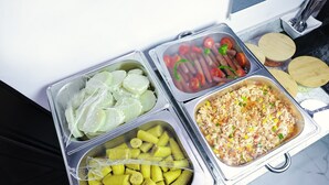 Un buffet proposant divers plats, notamment des tranches de concombre, des tomates et un plat contenant des légumes coupés en dés.