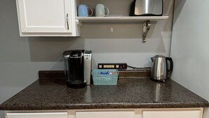 Cuina compacta amb armaris blancs, cafetera, bullidor i cistella al taulell.
