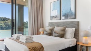 Une chambre d’hôtel avec un lit, une table de chevet avec une lampe, une vue sur un balcon et deux tableaux abstraits accrochés au mur.