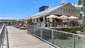 Un restaurant situé au bord de l’eau, appelé « FABRIC », doté d’une terrasse et d’une plateforme en bois.
